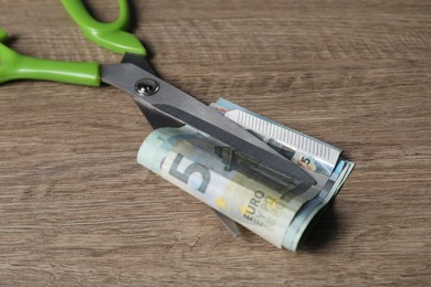 Photo of Euro banknotes and scissors on wooden table, closeup