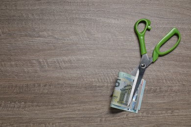 Photo of Euro banknotes and scissors on wooden table, top view. Space for text