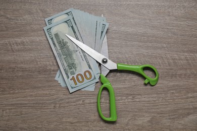 Photo of Dollar banknotes and scissors on wooden table, top view