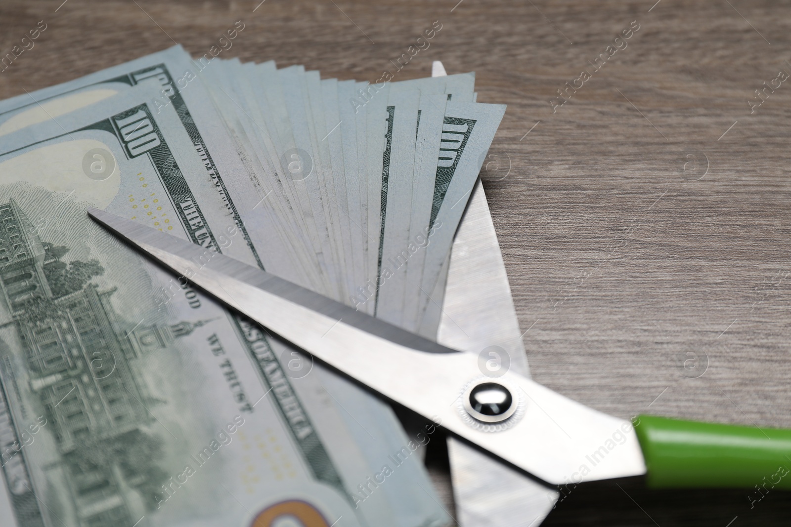 Photo of Dollar banknotes and scissors on wooden table, closeup