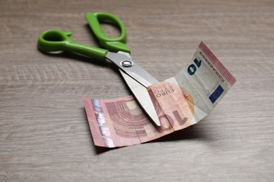 Photo of Euro banknote and scissors on wooden table, closeup