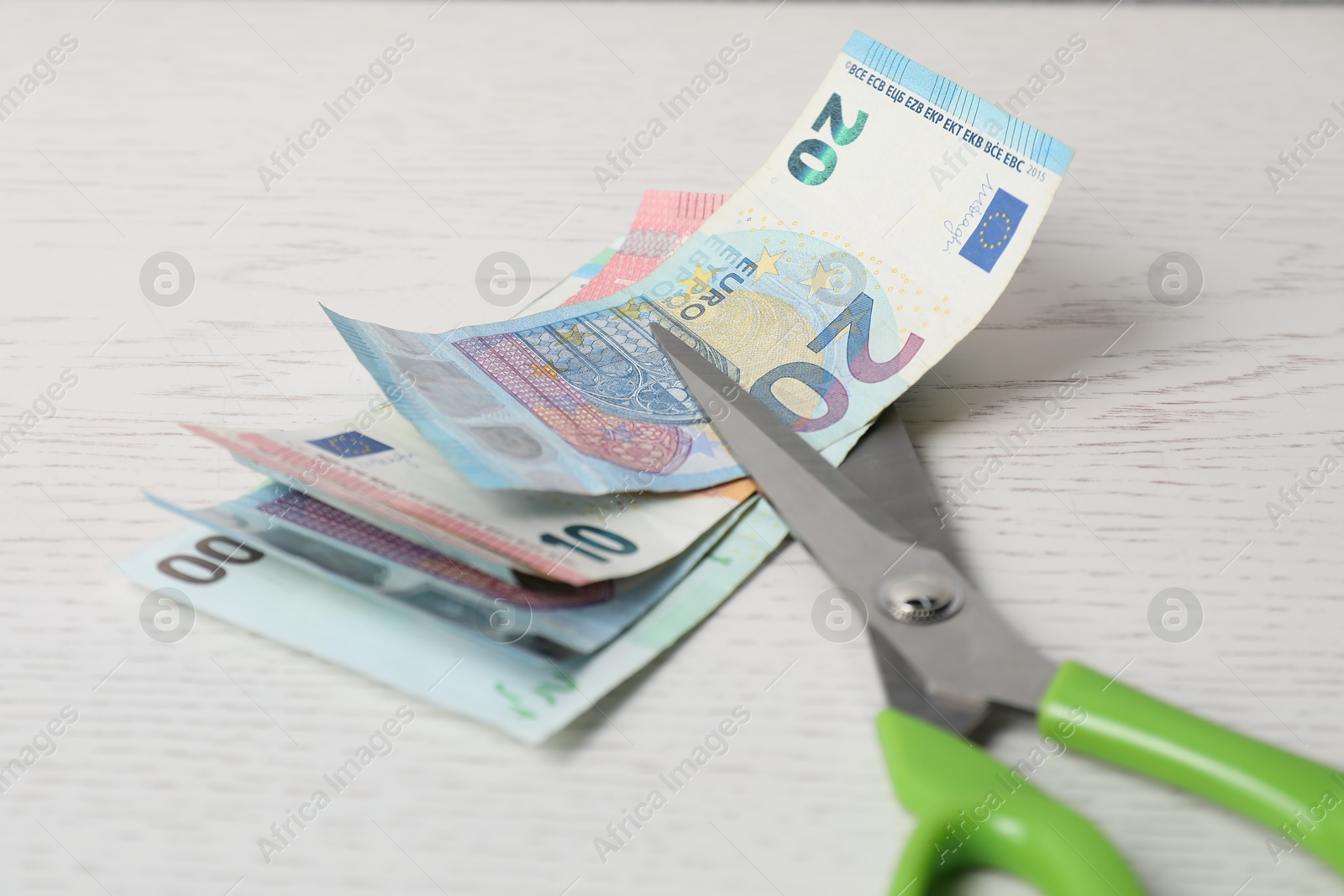 Photo of Euro banknotes and scissors on white wooden table, closeup