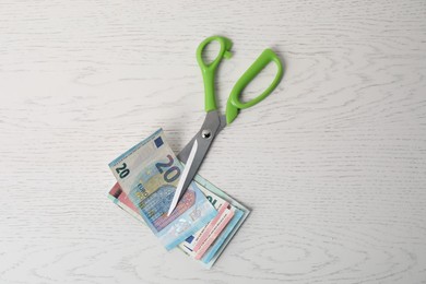 Photo of Euro banknotes and scissors on white wooden table, top view