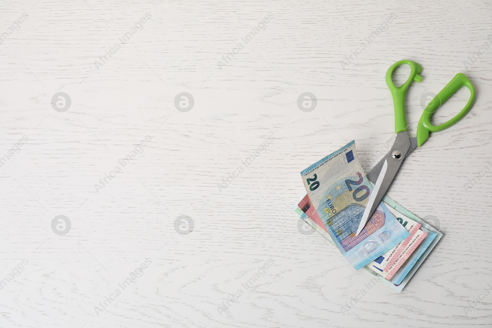 Photo of Euro banknotes and scissors on white wooden table, top view. Space for text