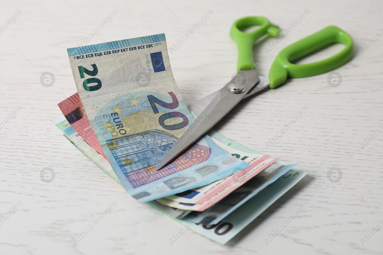 Photo of Euro banknotes and scissors on white wooden table, closeup