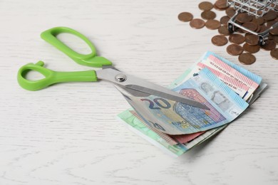 Photo of Euro banknotes, scissors and coins on white wooden table, closeup