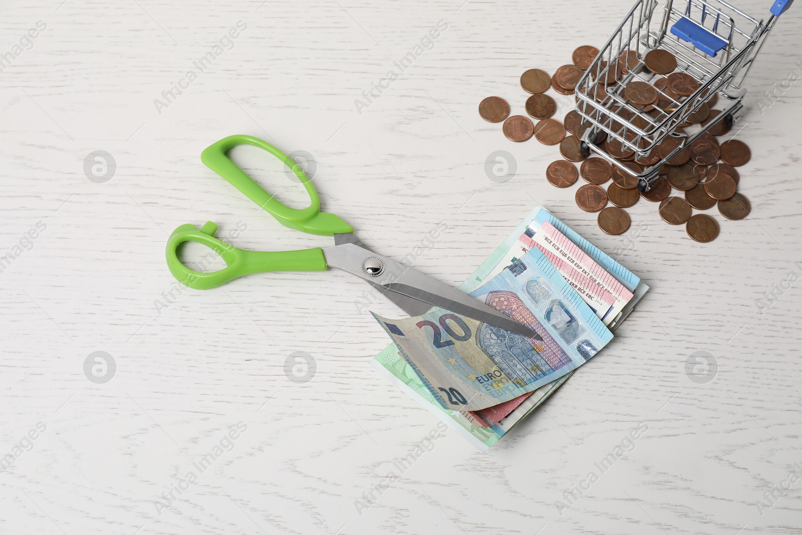 Photo of Euro banknotes, scissors and coins on white wooden table, flat lay