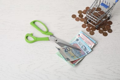 Photo of Euro banknotes, scissors and coins on white wooden table, flat lay