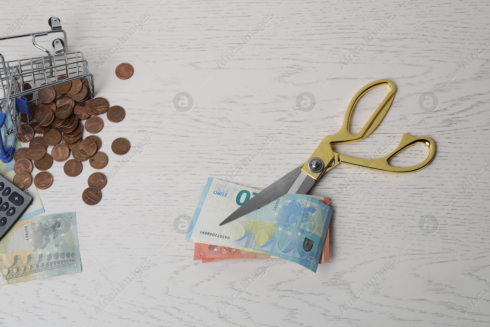 Photo of Euro banknotes, scissors and coins on white wooden table, flat lay