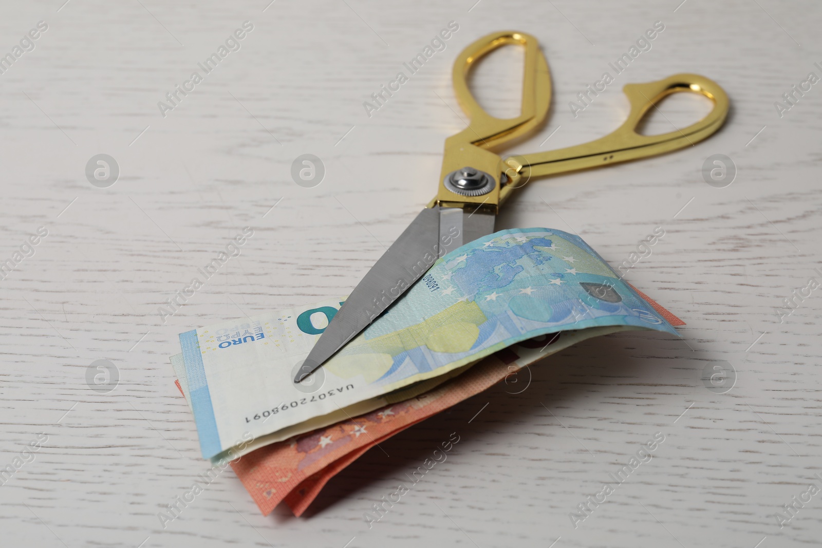 Photo of Euro banknotes and scissors on white wooden table, closeup