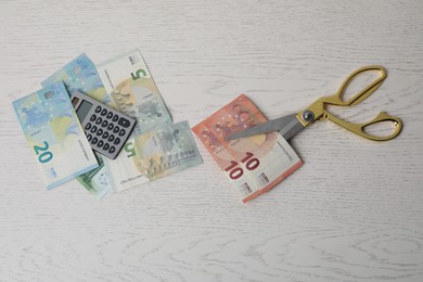 Photo of Euro banknotes, calculator and scissors on white wooden table, flat lay