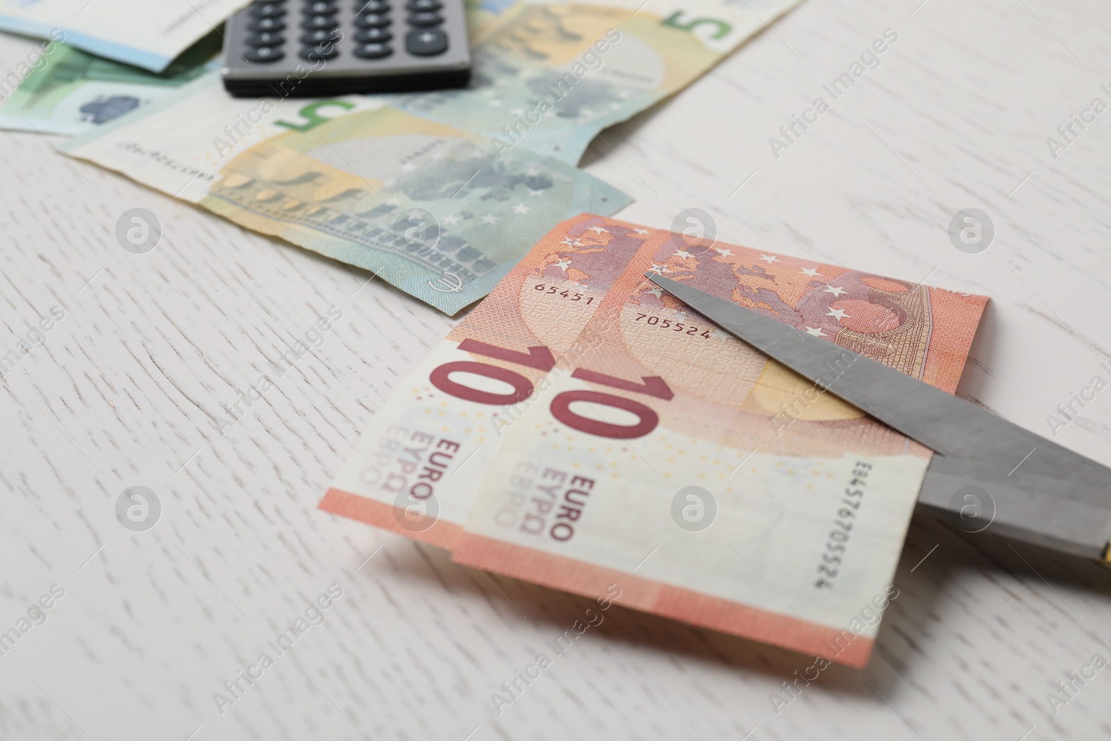 Photo of Euro banknotes and scissors on white wooden table, closeup