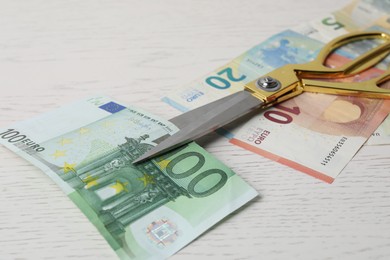 Photo of Euro banknotes and scissors on white wooden table, closeup