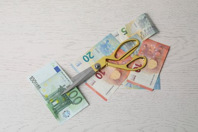 Photo of Euro banknotes and scissors on white wooden table, flat lay