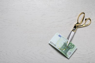 Photo of Scissors with euro banknote on white wooden table, top view. Space for text