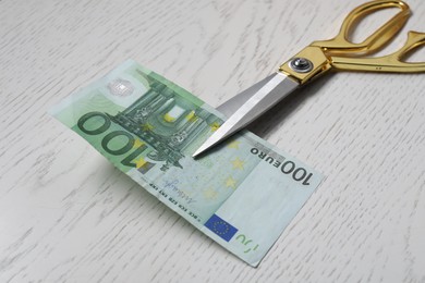 Photo of Scissors with euro banknote on white wooden table, closeup