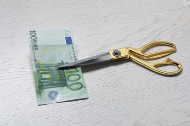 Photo of Scissors with euro banknote on white wooden table, closeup