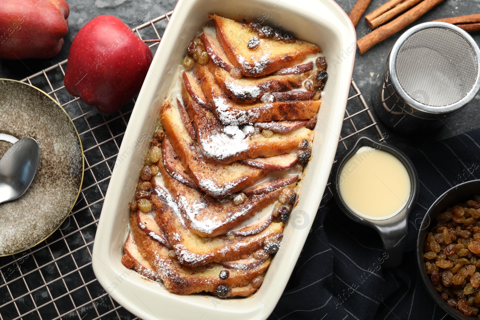 Photo of Freshly baked bread pudding in baking dish and products on grey textured table, flat lay