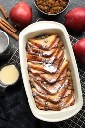 Photo of Freshly baked bread pudding in baking dish and products on grey textured table, flat lay