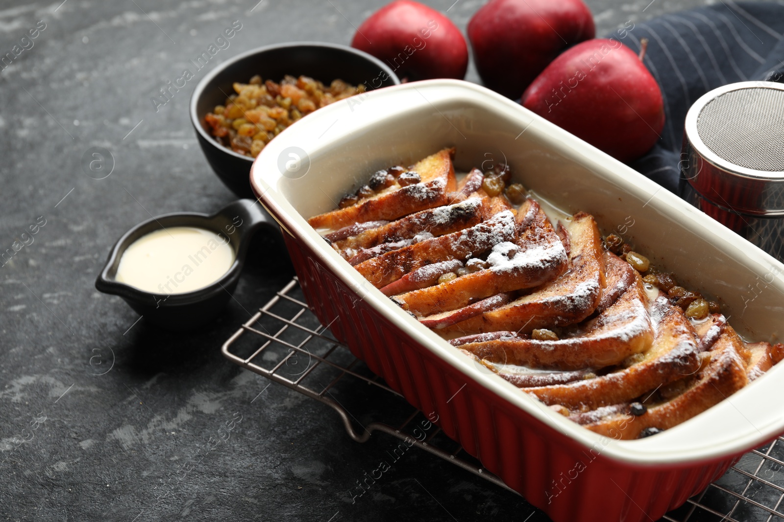 Photo of Freshly baked bread pudding in baking dish and products on dark textured table, closeup