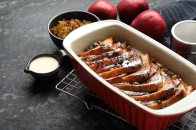 Photo of Freshly baked bread pudding in baking dish and products on dark textured table, closeup