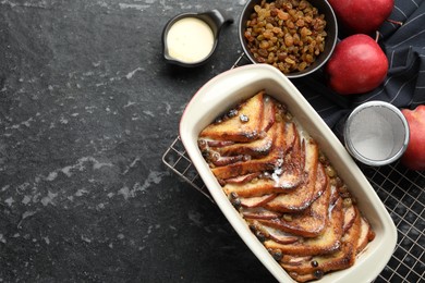 Photo of Freshly baked bread pudding in baking dish and products on grey textured table, flat lay. Space for text