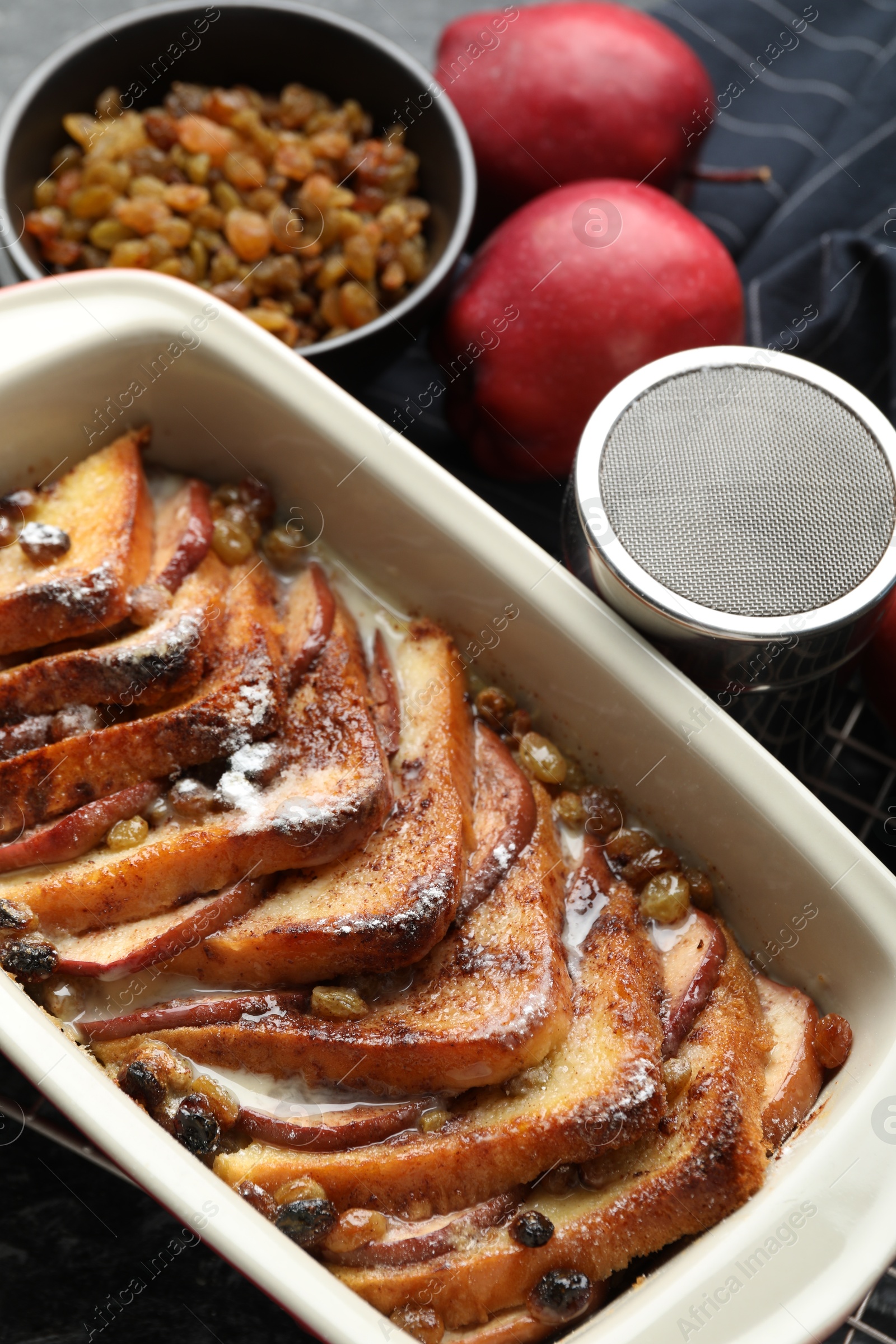 Photo of Freshly baked bread pudding in baking dish, apples and raisins on table, above view