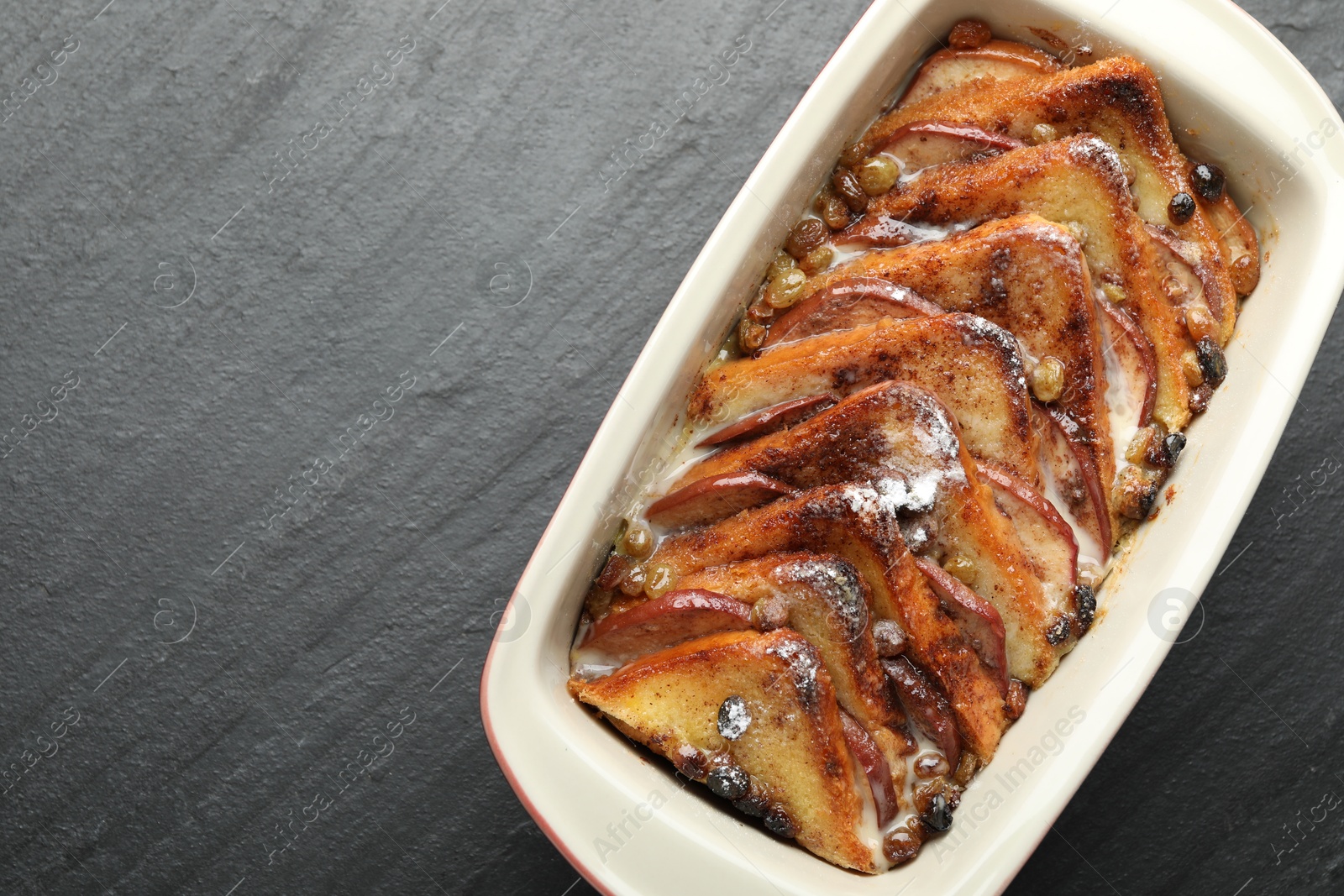 Photo of Freshly baked bread pudding in baking dish on grey textured table, top view. Space for text