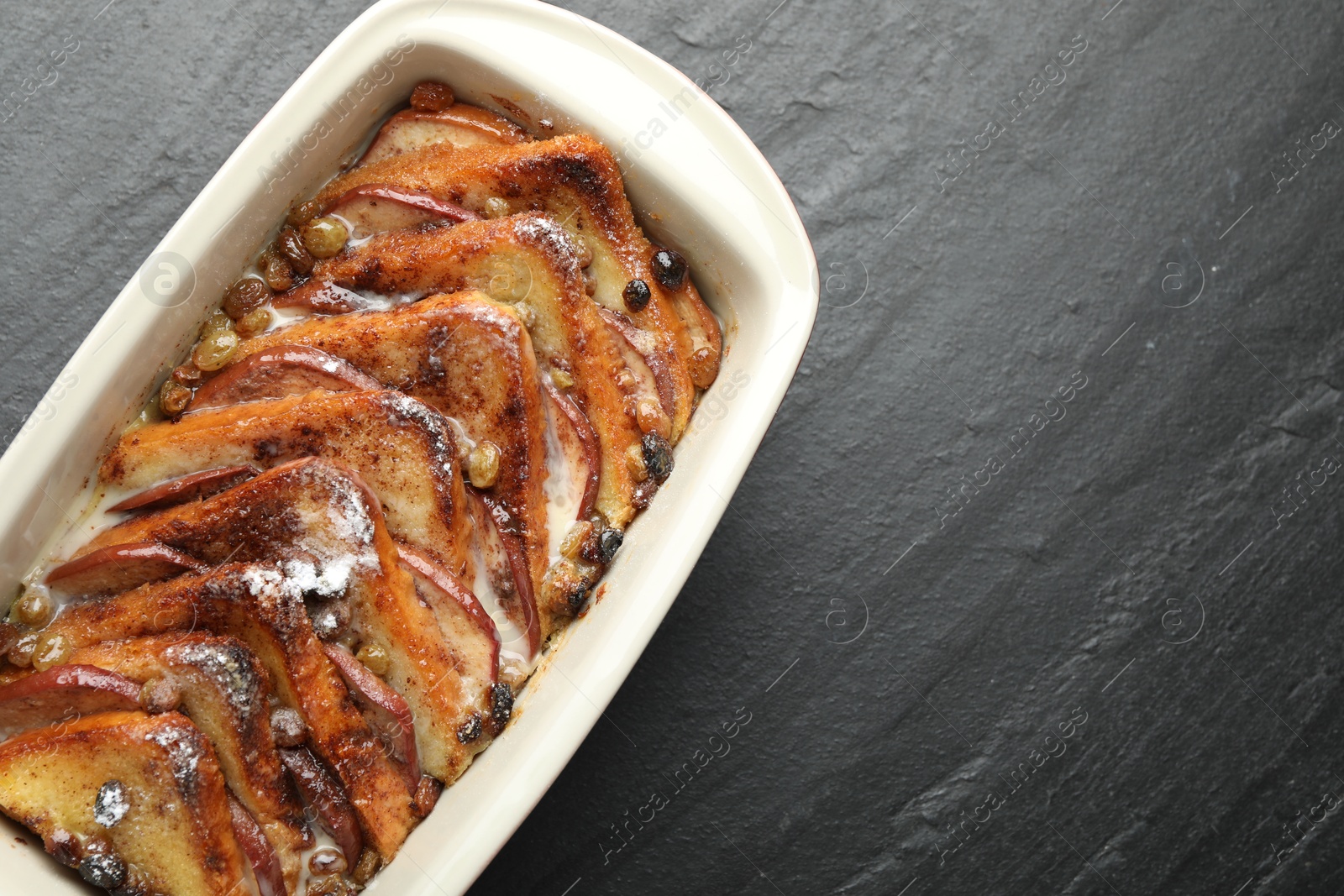 Photo of Freshly baked bread pudding in baking dish on grey textured table, top view. Space for text