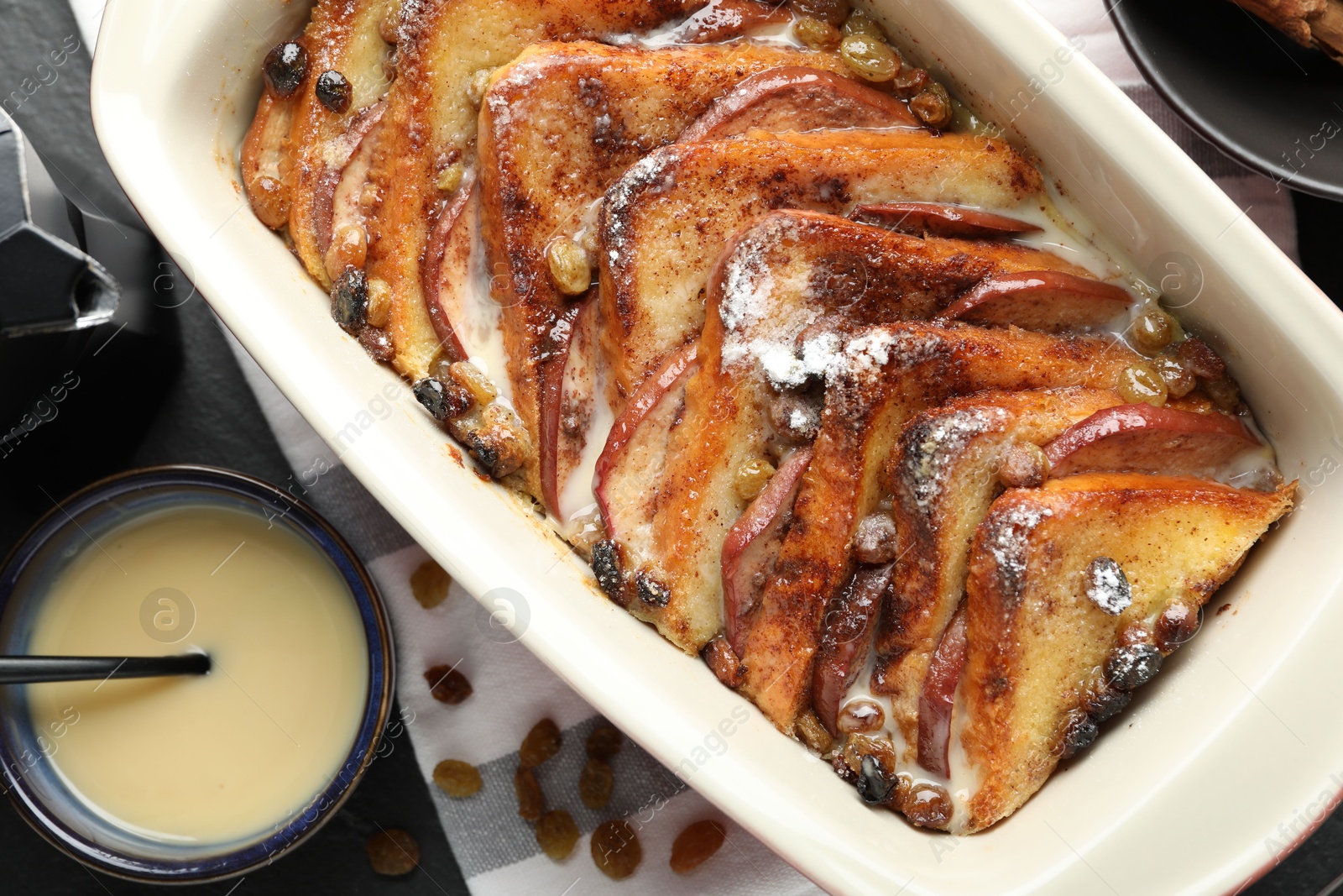 Photo of Freshly baked bread pudding and custard cream on dark table, flat lay