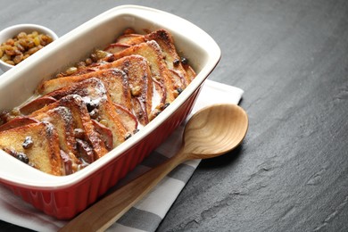 Photo of Freshly baked bread pudding in baking dish and wooden spoon on dark textured table, closeup. Space for text