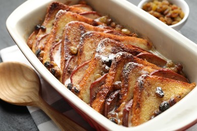 Photo of Freshly baked bread pudding in baking dish and wooden spoon on dark table, closeup