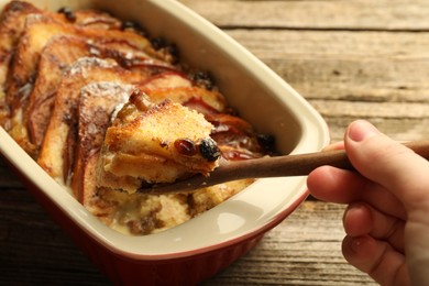 Photo of Woman eating tasty bread pudding at wooden table, closeup