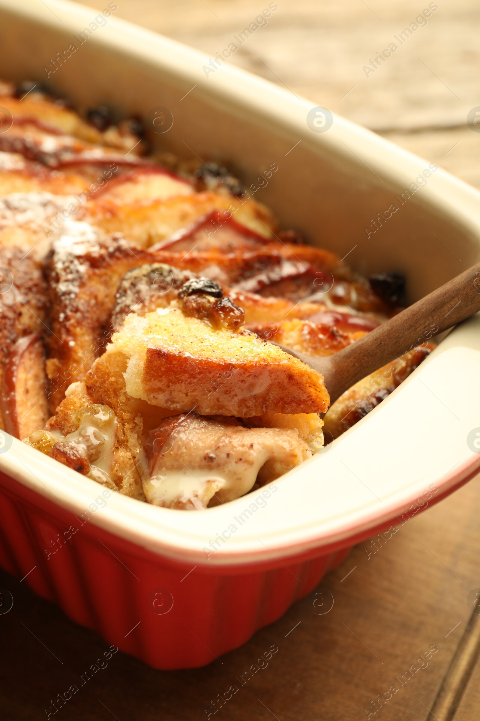 Photo of Taking tasty bread pudding from baking dish at wooden table, closeup