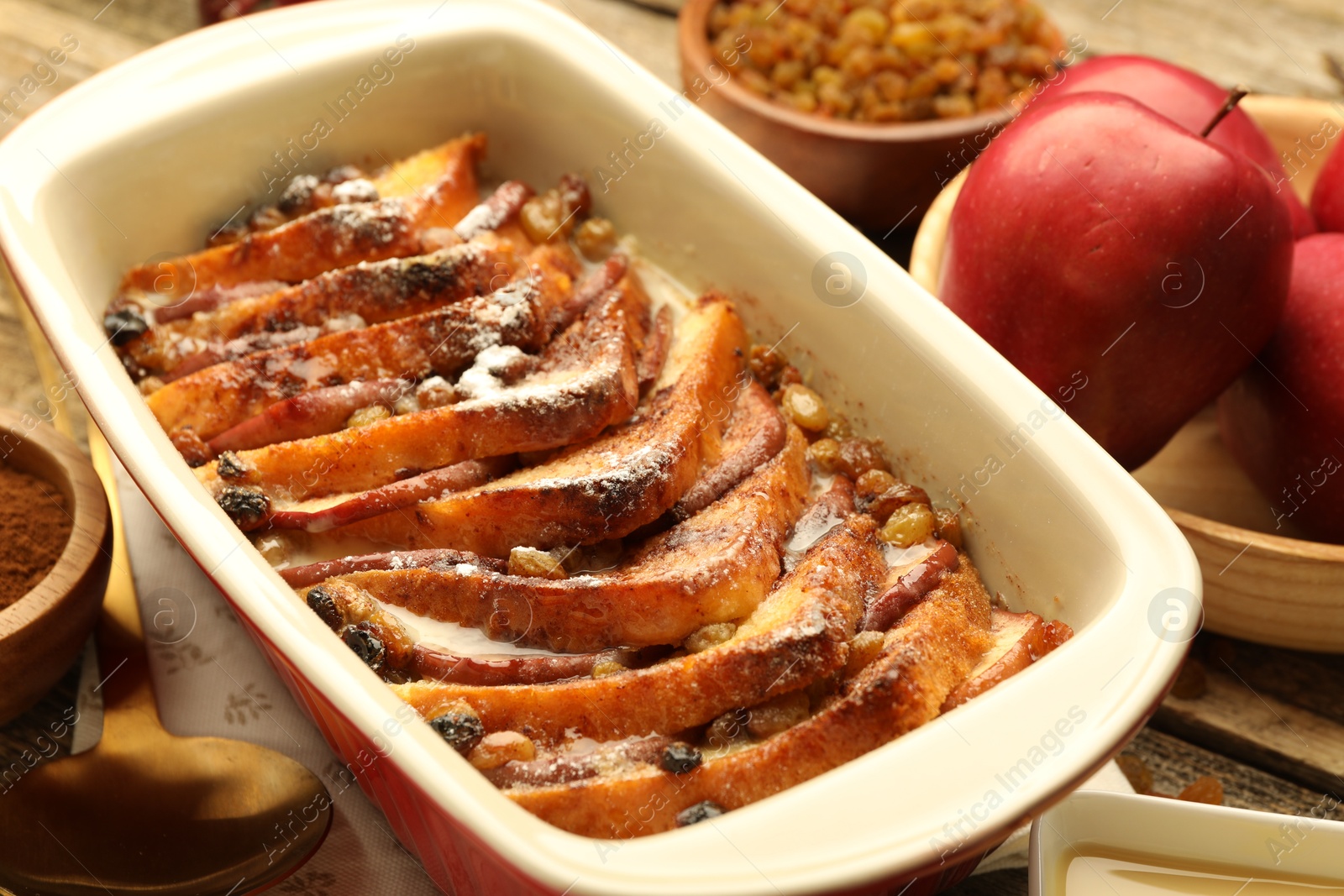 Photo of Freshly baked bread pudding in baking dish and apples on table, closeup