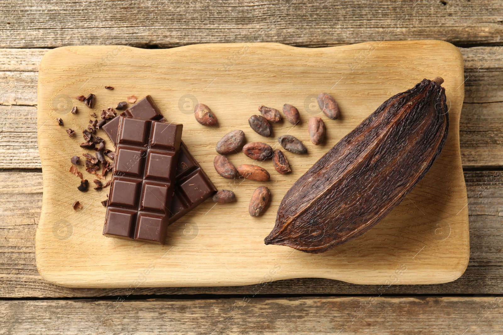 Photo of Cocoa pod, beans and chocolate on wooden table, top view