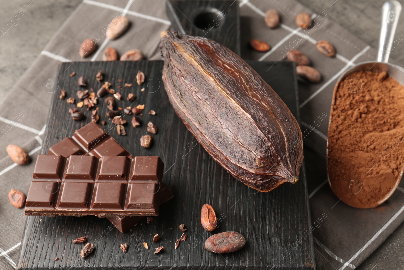 Photo of Cocoa pod, beans, powder and chocolate on grey table, closeup