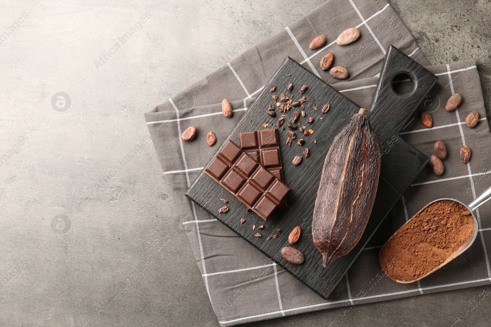 Photo of Cocoa pod, beans, powder and chocolate on grey table, flat lay