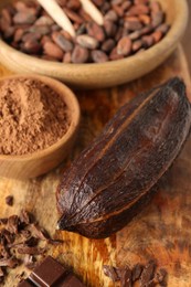 Cocoa pod, beans, powder and chocolate on wooden table, closeup