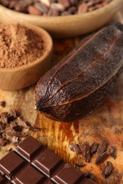 Photo of Cocoa pod, beans, powder and chocolate on wooden table, closeup