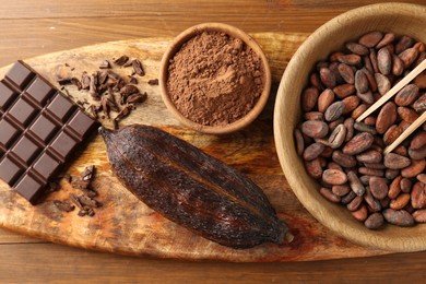 Photo of Cocoa pod, beans, powder and chocolate on wooden table, top view