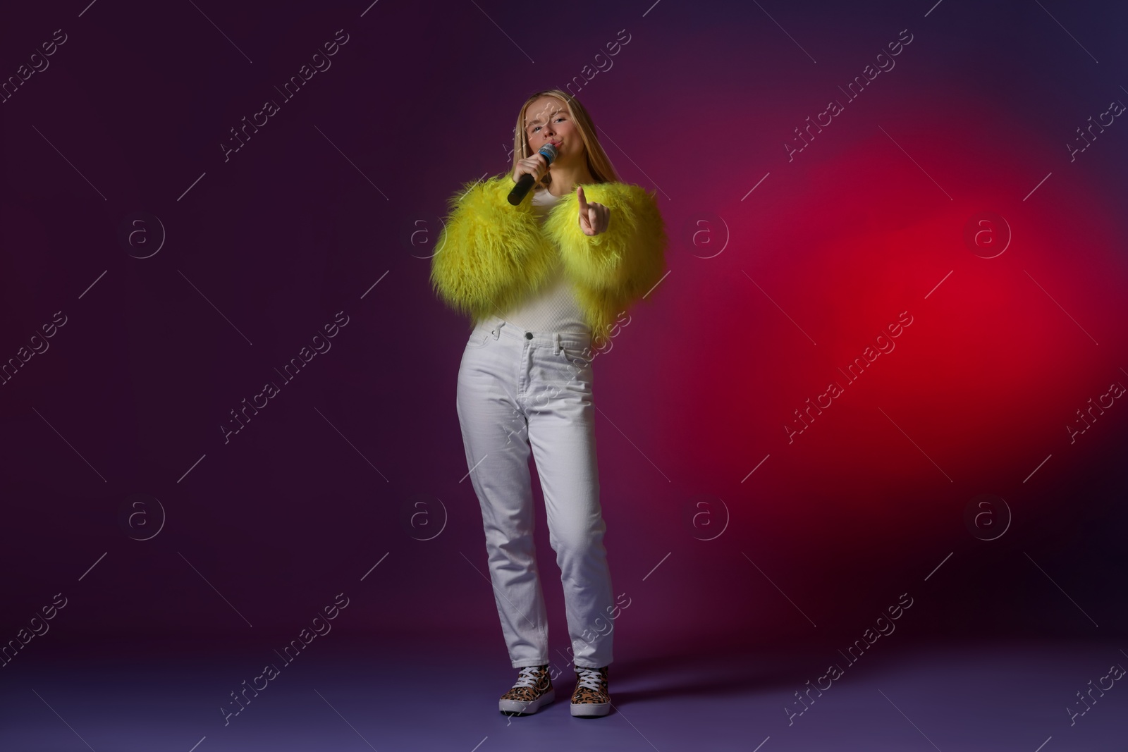 Photo of Talented singer in faux fur performing on dark background with pink light