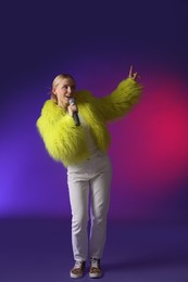 Photo of Talented singer in faux fur performing on purple background with pink light