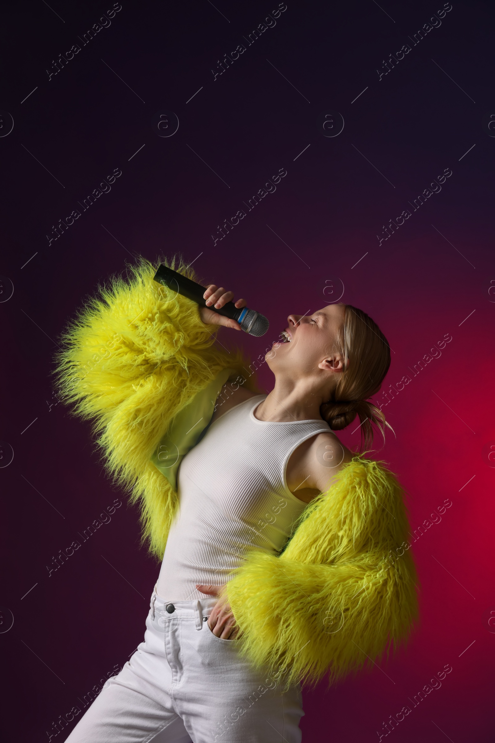 Photo of Talented singer in faux fur performing on dark background with pink light