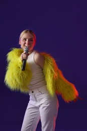 Photo of Talented singer in bright faux fur coat performing on purple background. Space for text