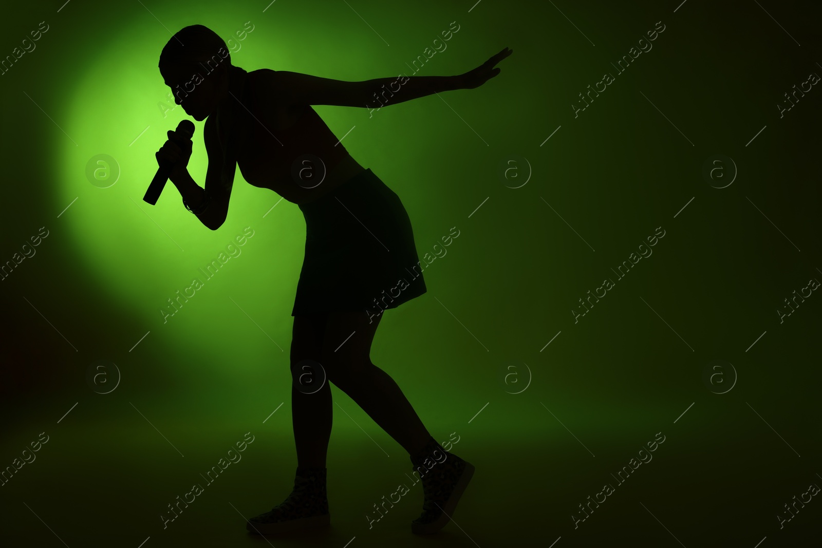 Photo of Silhouette of woman singing on dark background with green light. Space for text