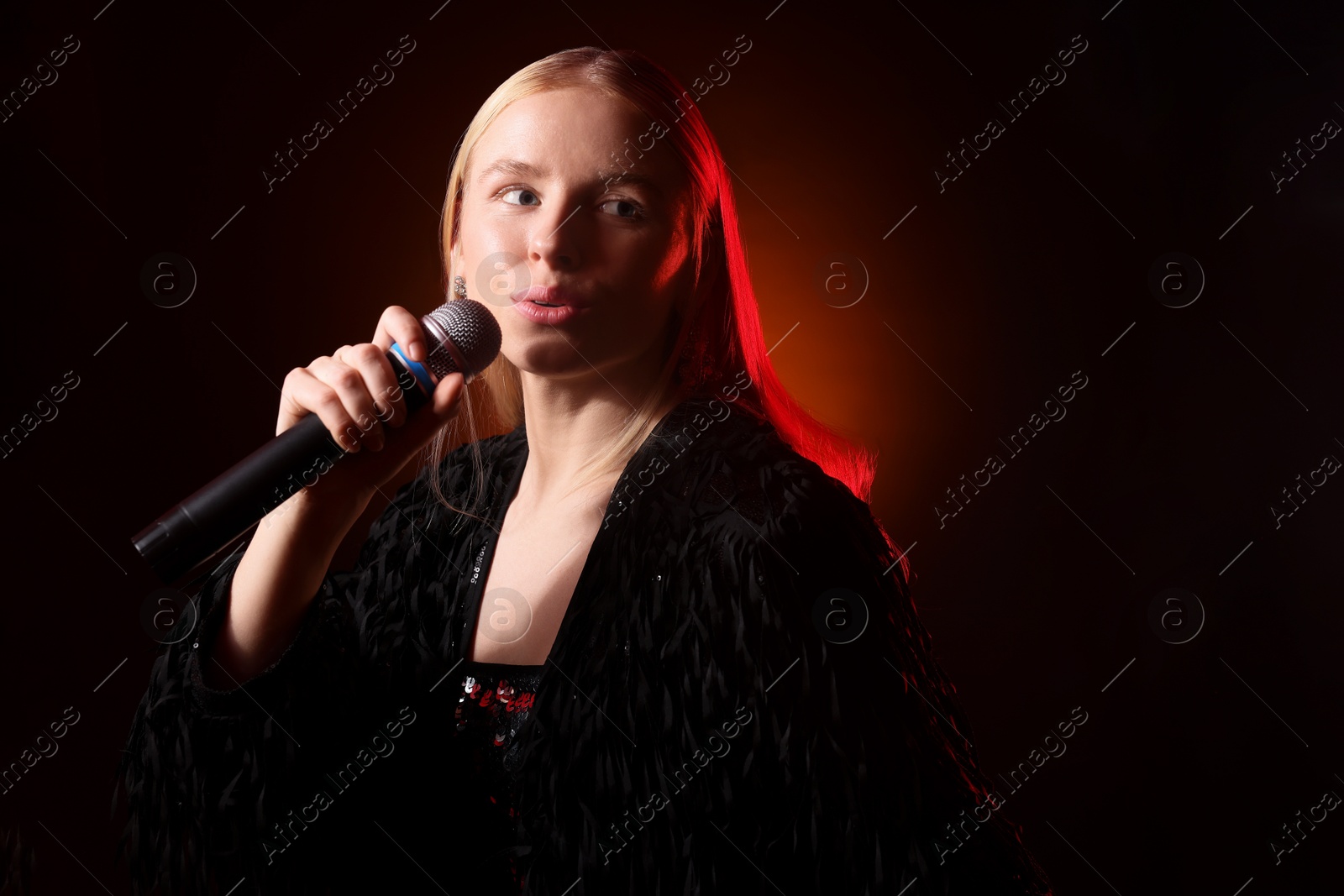 Photo of Beautiful singer performing on dark background with orange light. Space for text