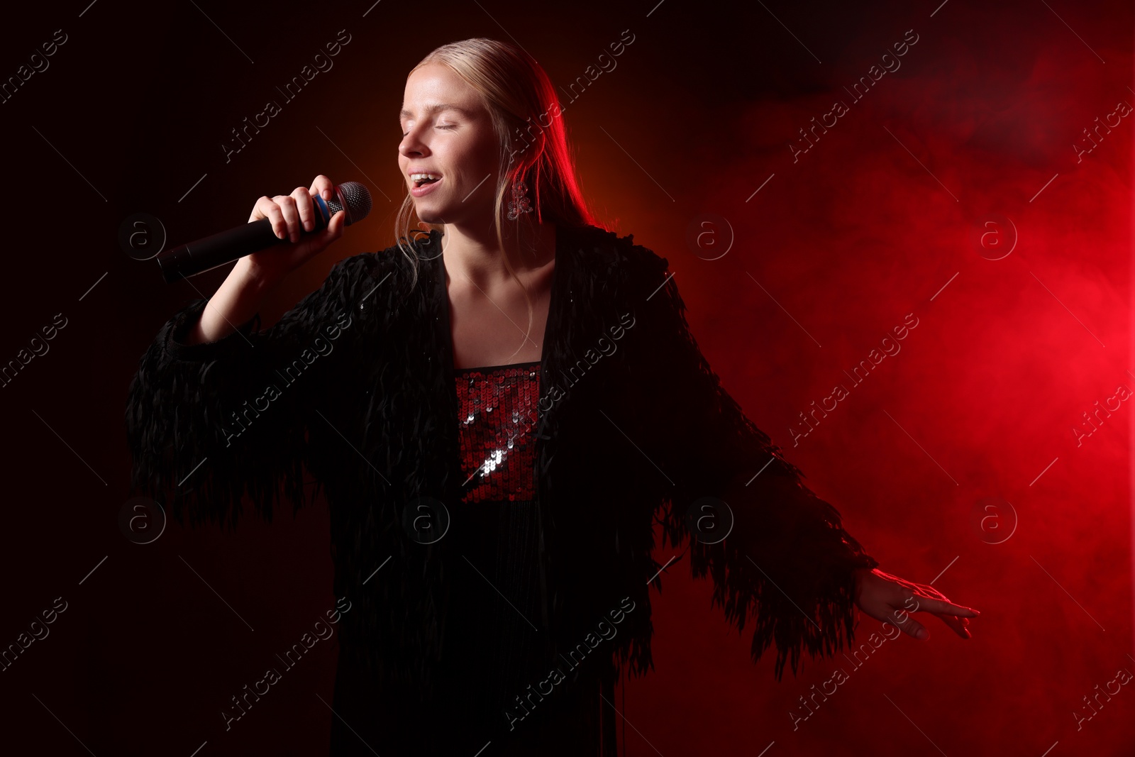 Photo of Beautiful singer performing on dark background with red light and smoke