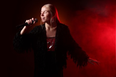 Photo of Beautiful singer performing on dark background with red light and smoke