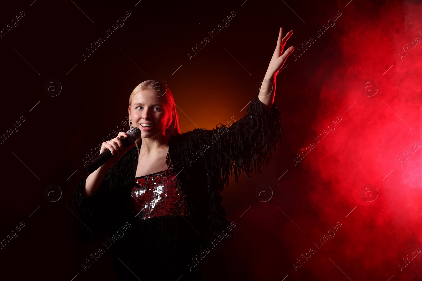 Photo of Beautiful singer performing on dark background with red light and smoke